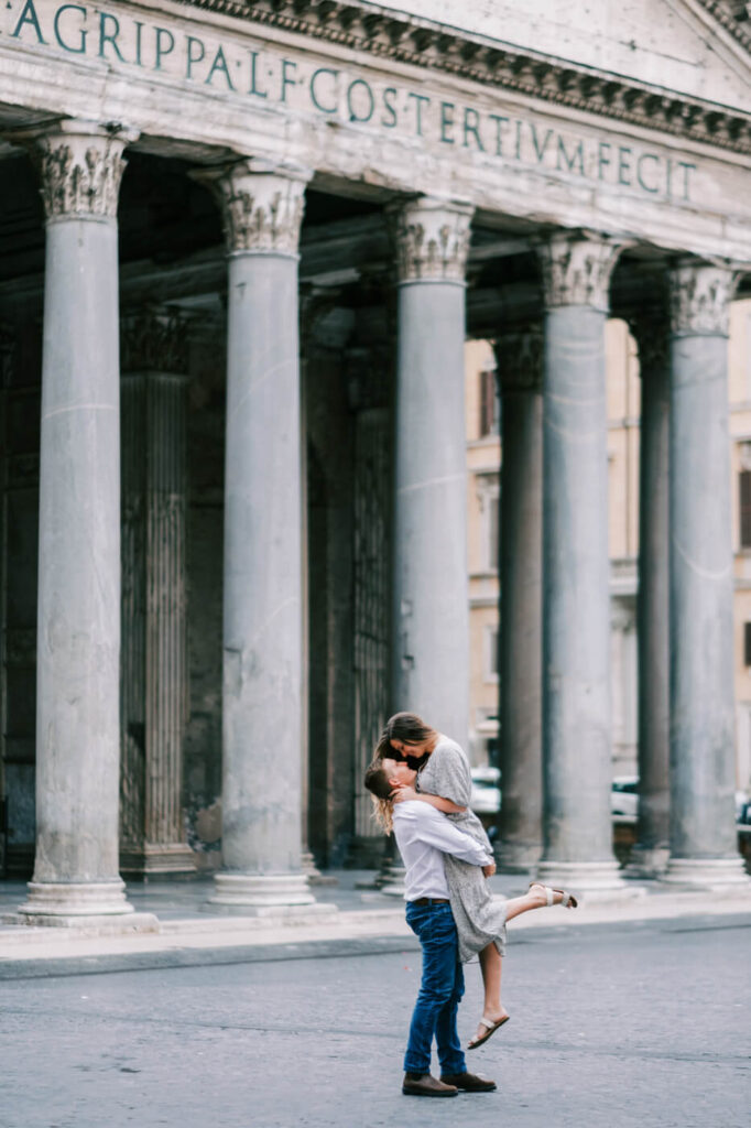 Romantic embrace at the Pantheon, Rome – A couple shares a joyful kiss as the man lifts his partner in front of the iconic Pantheon, with its grand columns and historic inscription framing their love-filled moment.