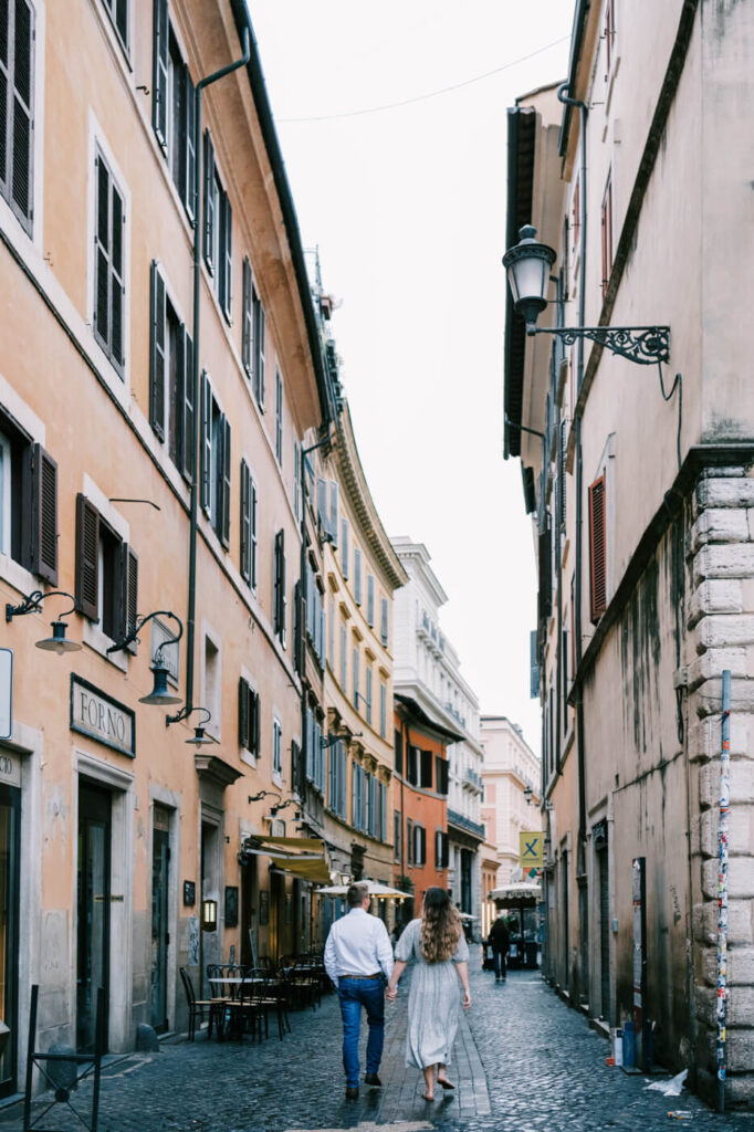 Strolling through Rome’s cobblestone streets – The couple walks hand in hand down a charming cobblestone street in Rome, lined with warm-hued buildings, shuttered windows, and classic Italian cafés.