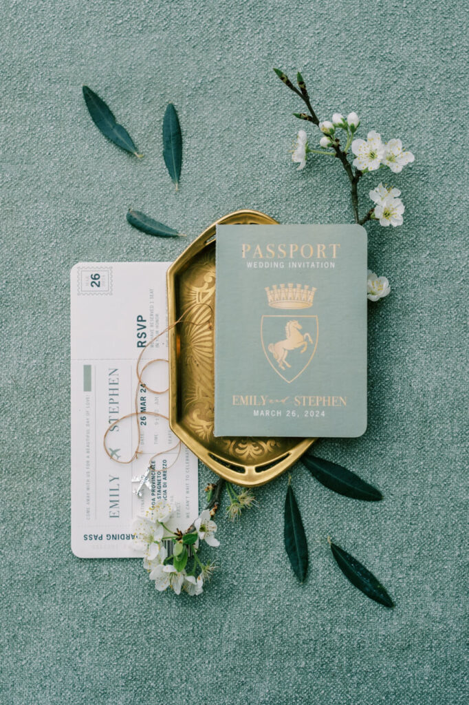 Elegant wedding invitation suite with a passport-style design for a destination wedding in Tuscany, featuring gold details and olive branch accents.