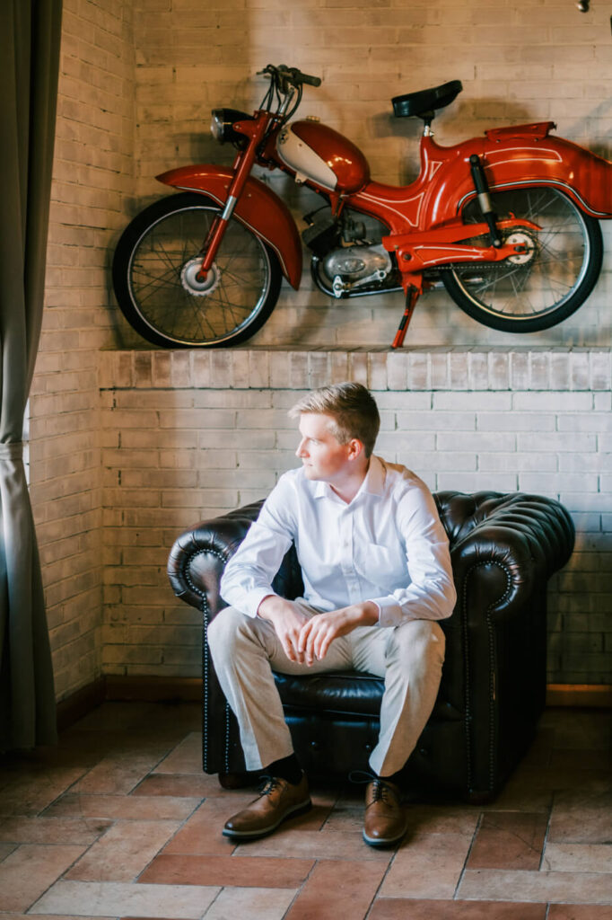 The groom relaxes in a leather armchair at Villa Olimpia, Tuscany, before his intimate destination wedding in Italy.