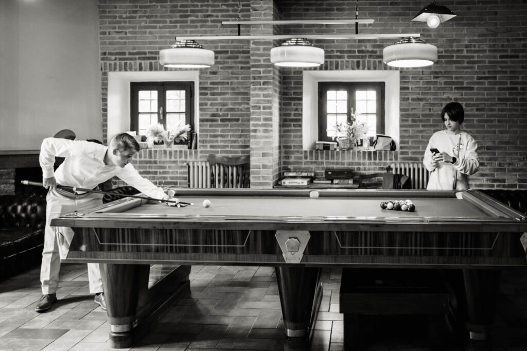 Groom playing pool in a Tuscany villa game room, featuring exposed brick walls and vintage decor.