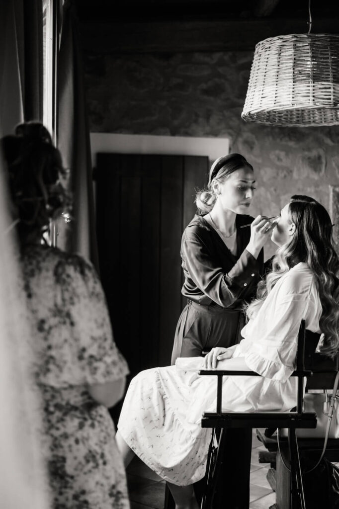 Bride getting her makeup done in soft natural light, surrounded by rustic stone walls in a Tuscany villa.