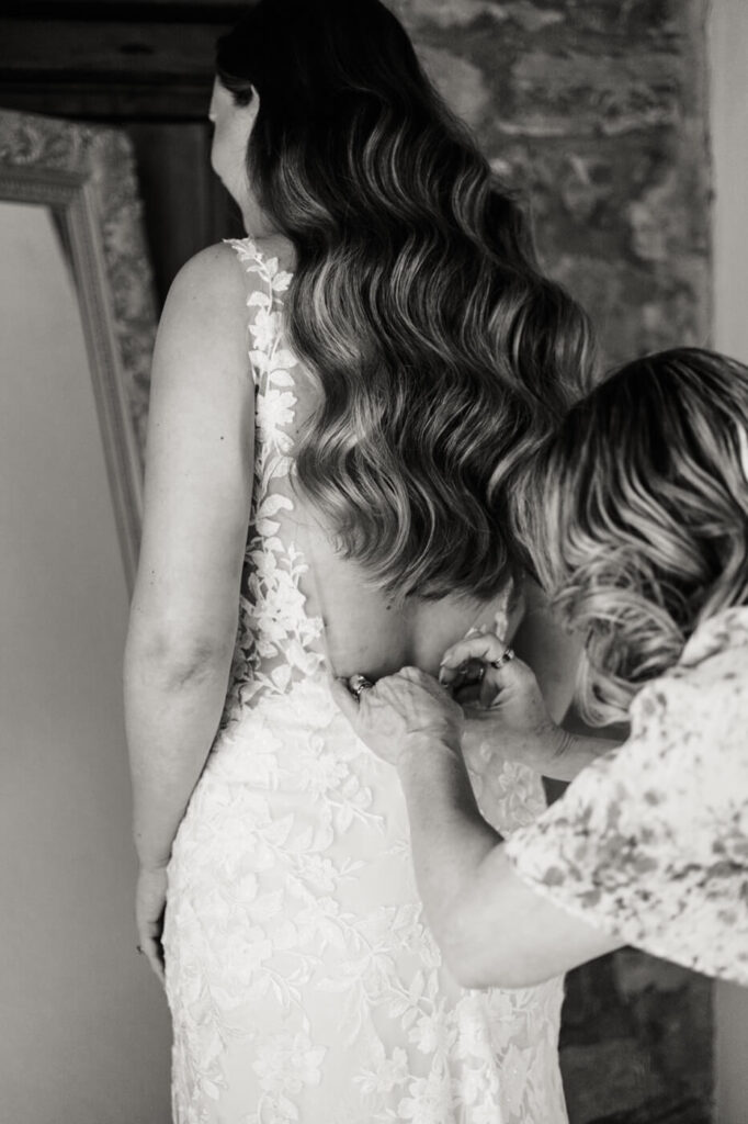 Bride’s delicate lace wedding gown being buttoned up, showcasing intricate floral embroidery.