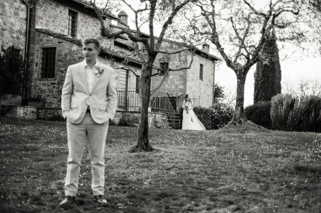 Bride approaching the groom for an emotional first look, framed by Tuscany villa stone walls and olive trees.