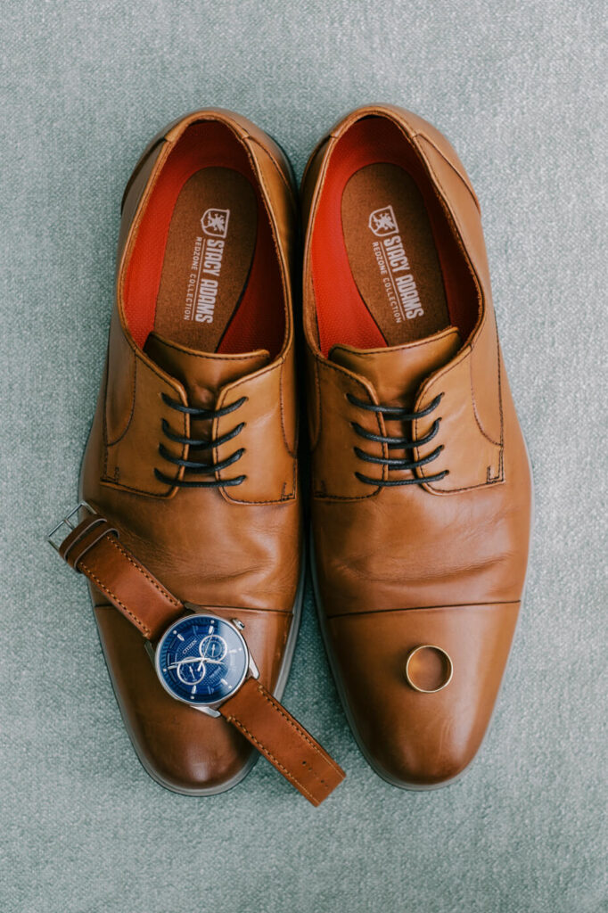 Stylish groom’s wedding details, including classic brown leather shoes, a navy blue watch, and a gold wedding band, captured before the Tuscany villa ceremony.