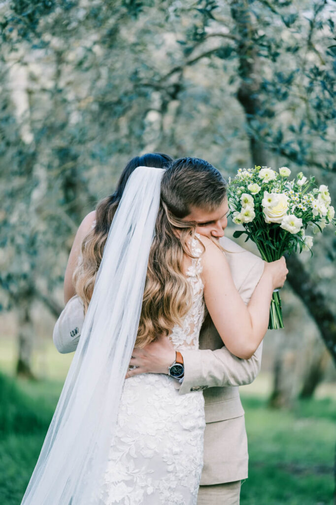 Bride and groom embracing in an olive grove, a romantic first look moment at their Tuscany wedding.