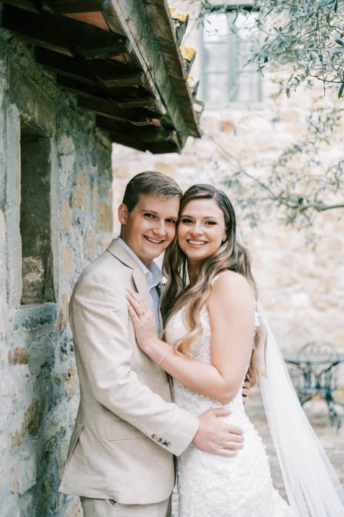 The couple smiles before their ceremony, wrapped in each other’s arms next to Tuscan villa.