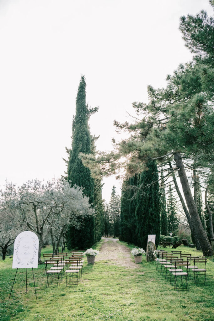 Wedding ceremony at Villa Olimpia in Tuscany with elegant floral arrangements and towering cypress trees lining the aisle.