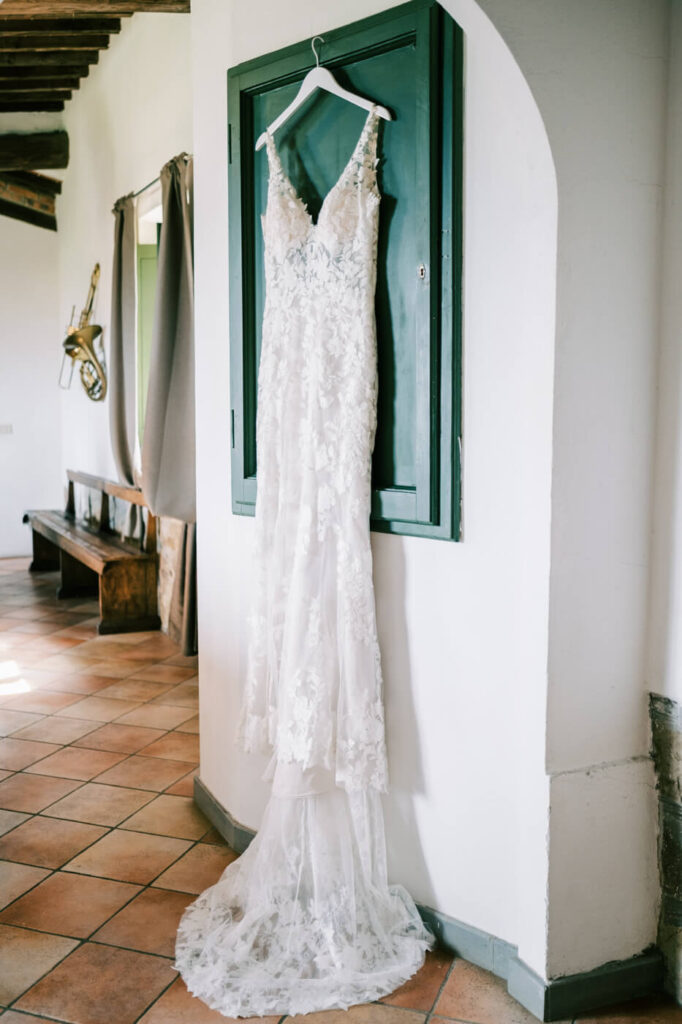 Romantic lace wedding dress hanging inside Villa Olimpia, an intimate Tuscany wedding venue, before the bride’s elegant destination wedding.