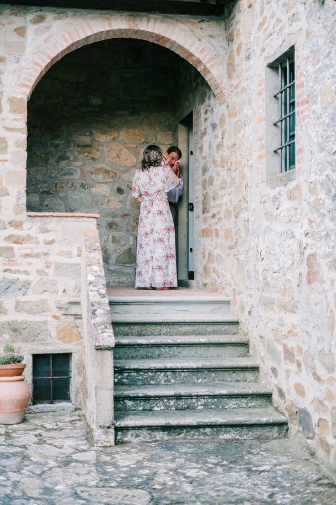 Father wiping away tears while the mother looks on, framed by the rustic charm of the Tuscany villa courtyard.