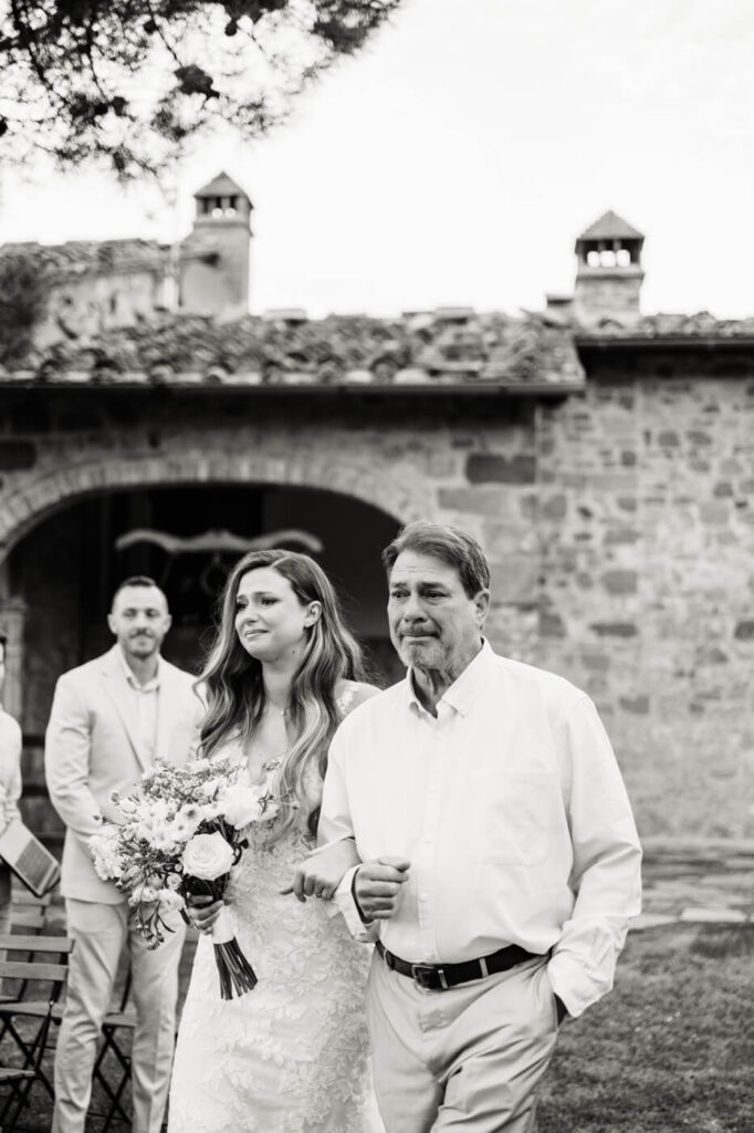 Bride walking arm in arm with her father, her expression filled with emotion as they make their way to the ceremony.