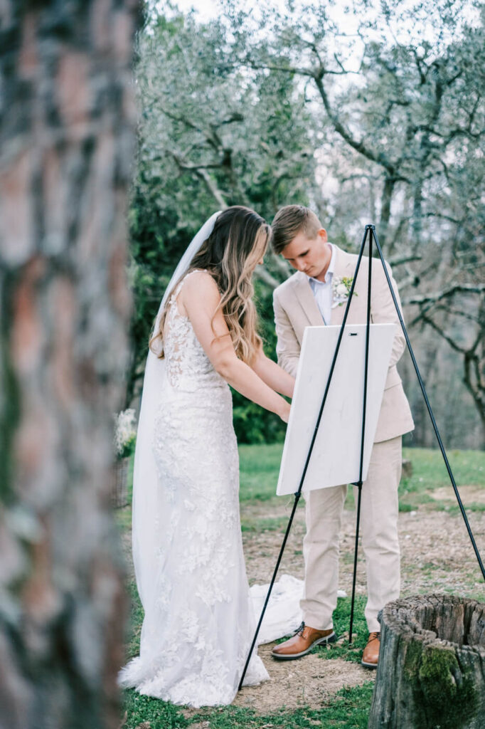 Bride and groom intertwining knots together under the olive trees, a moment of unity and commitment.