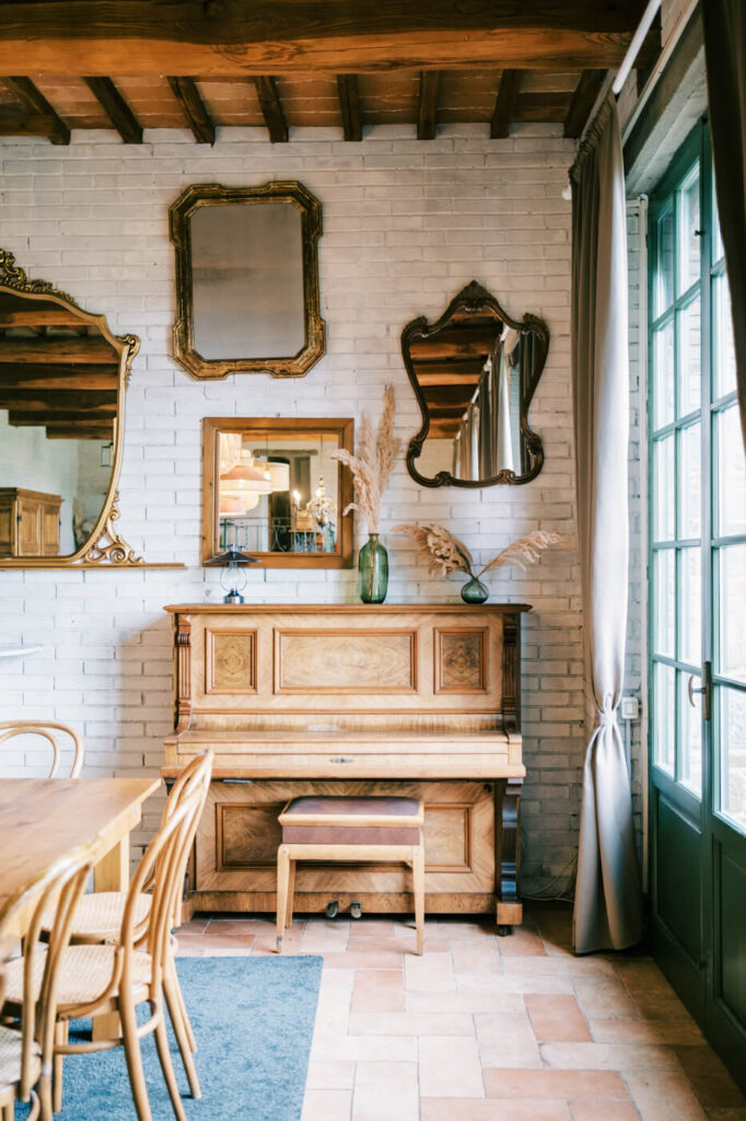 A vintage wooden piano with antique mirrors on a white brick wall inside Villa Olimpia, a romantic Tuscany wedding venue.