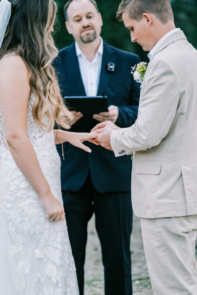 The exchange of rings—a groom delicately slips a wedding band onto his bride’s finger as the officiant looks on.