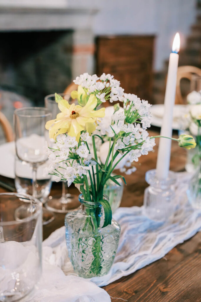 Ethereal tablescape details – A close-up of delicate wildflowers in glass vases, candlelight flickering around them, sets the tone for an intimate Italian dinner.