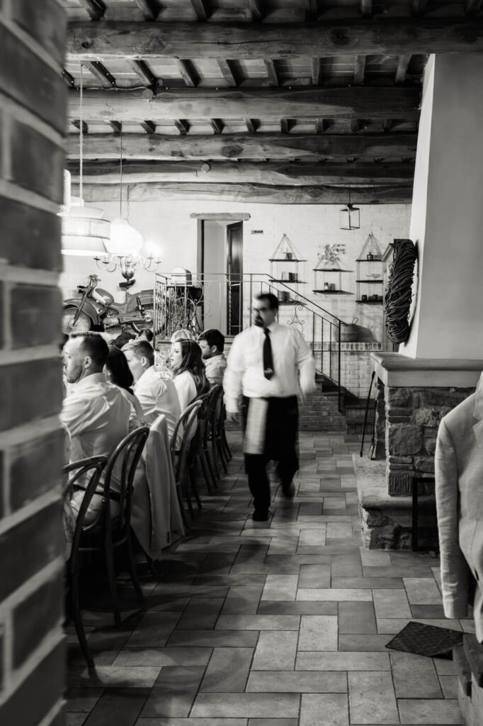 A timeless dining experience – A motion-filled black-and-white frame of a waiter serving guests, capturing the warmth and movement of the evening.