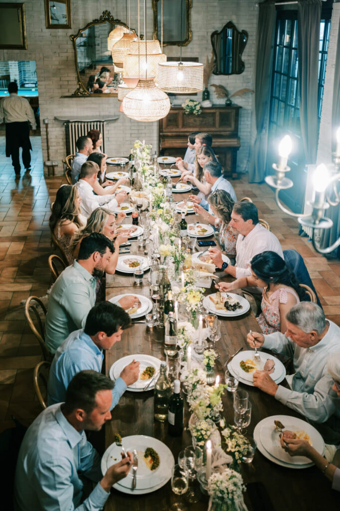 A long dining table adorned with white florals and candles, surrounded by wedding guests enjoying an intimate dinner at Villa Olimpia, Tuscany.