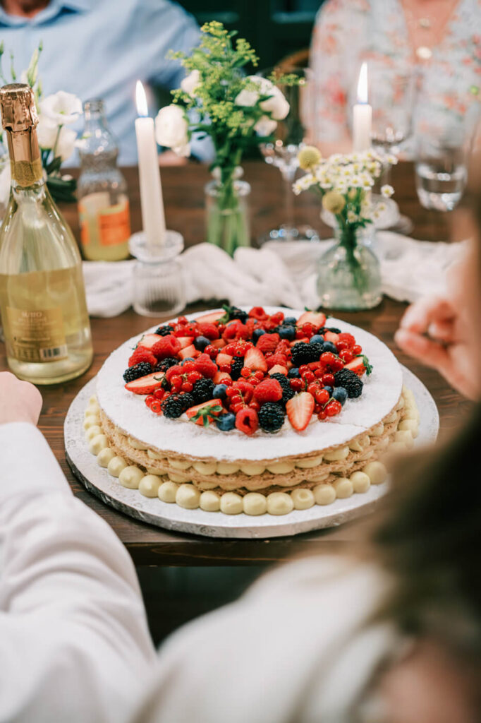 A stunning wedding cake topped with fresh berries and delicate cream puffs, surrounded by candlelight and floral arrangements.