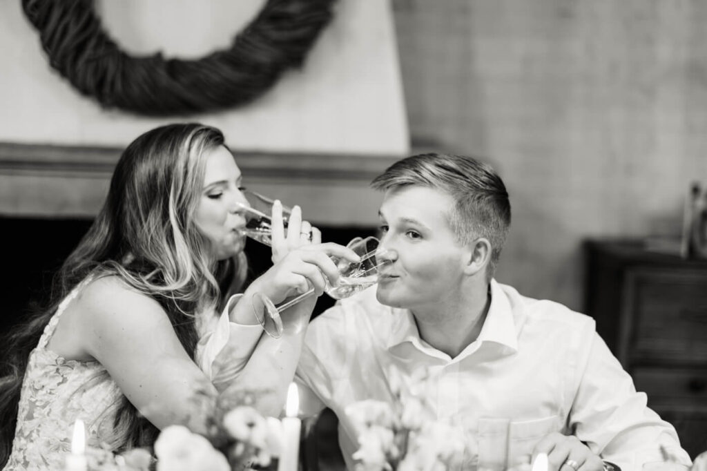 The bride and groom clink glasses in a playful and romantic toast, sharing a joyful moment.