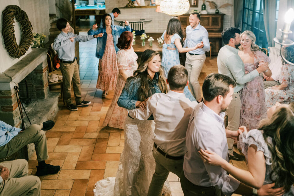 The bride and groom dance joyfully with their guests in a cozy, rustic Tuscan reception space.