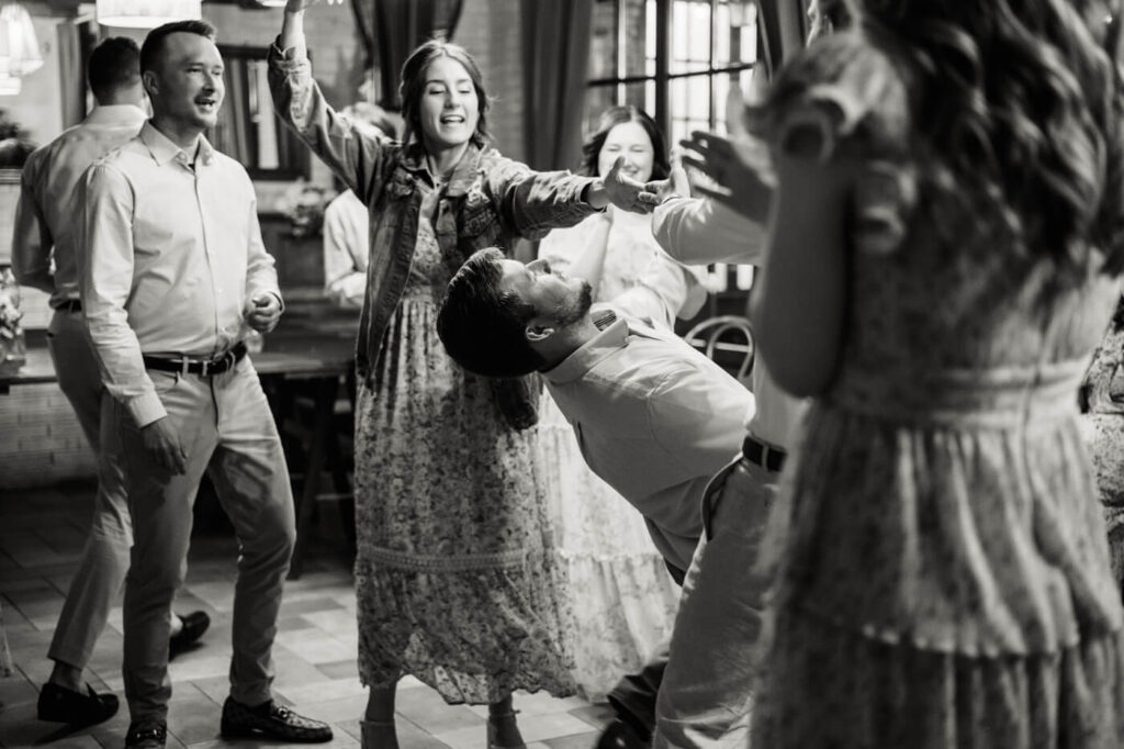 A lively black-and-white photo of wedding guests dancing, laughing, and celebrating together.