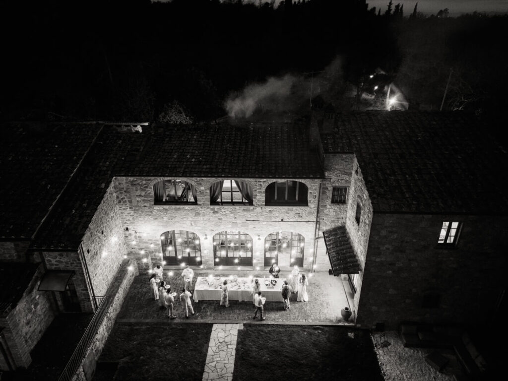 An enchanting reception under the stars – A black and white aerial shot of the villa’s courtyard, where guests gather for an intimate candlelit dinner, laughter and conversation filling the evening air.