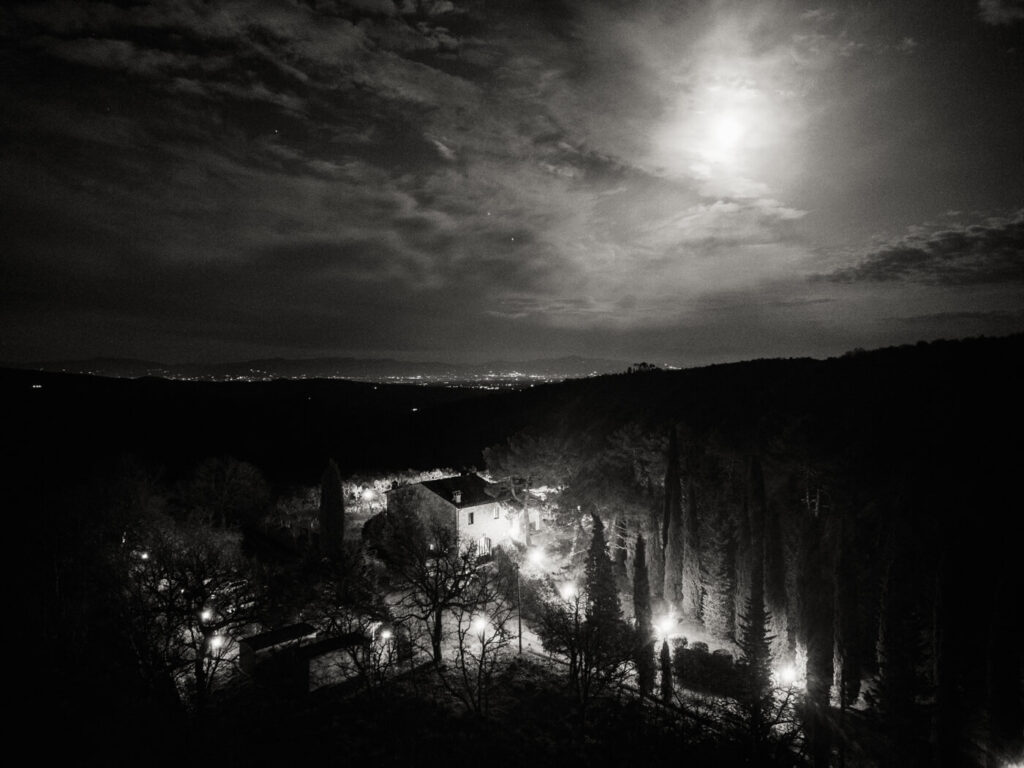 A magical Tuscan night at Villa Olimpia – A moonlit aerial view of the villa nestled among rolling hills, the warm glow of lights dotting the landscape.