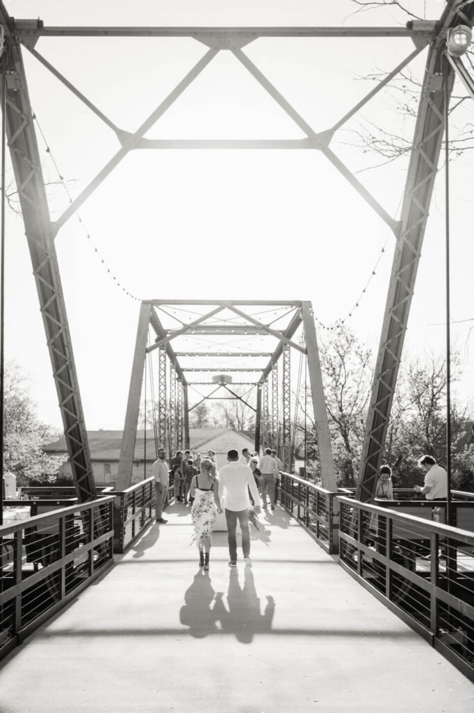 Black and White Photo of Couple Walking Across Finley Farm Bridge at Rehearsal Dinner – A romantic black and white capture of the couple strolling across Finley Farm Bridge as the sun sets.