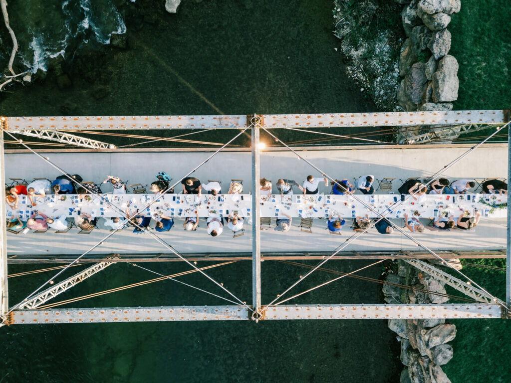 Aerial View of Rehearsal Dinner Table on Finley Farm Bridge Over River – A stunning drone shot showcases an elegant al fresco dinner setting atop Finley Farm Bridge, with the river flowing below.