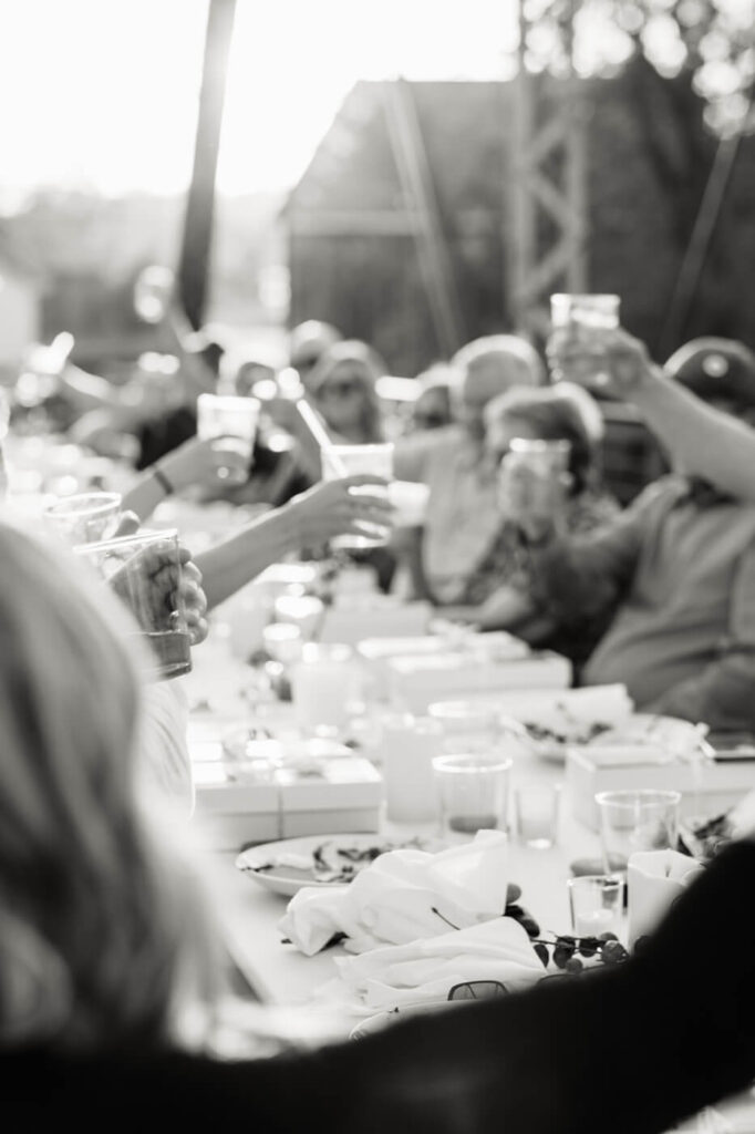 Black and White Image of Guests Toasting at Finley Farm Bridge Rehearsal Dinner – A timeless black and white capture of wedding guests raising glasses to celebrate love and new beginnings at Finley Farm Bridge.