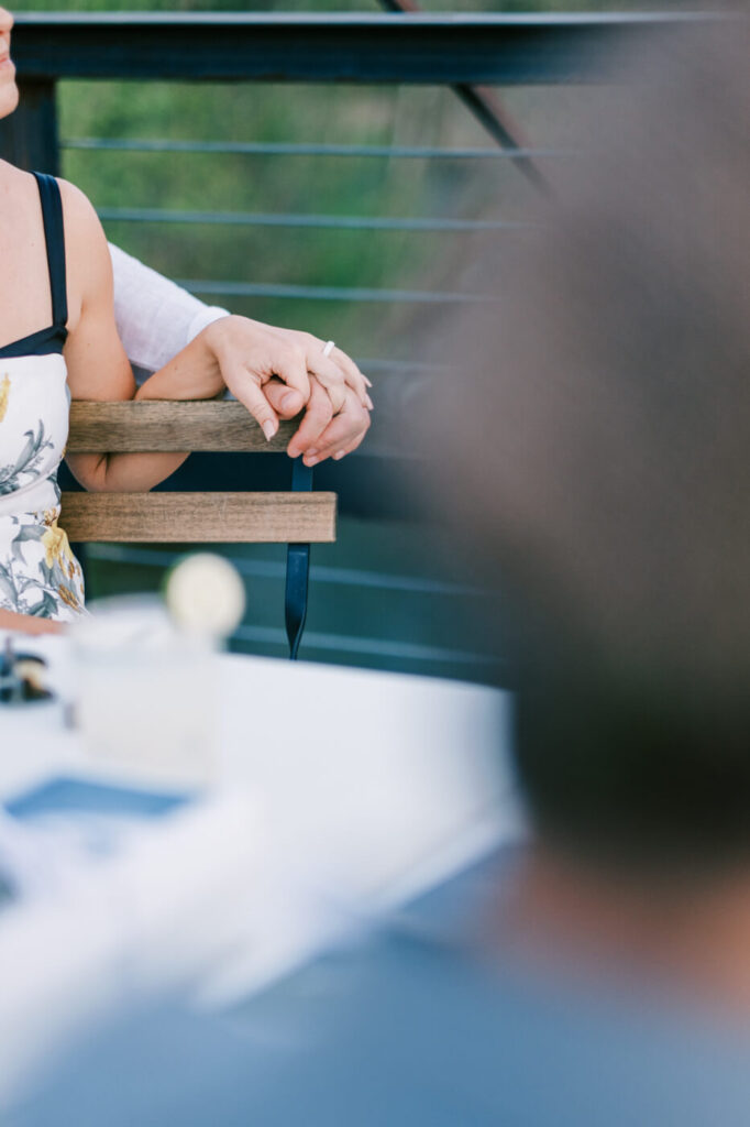 Couple Holding Hands During Toast at Finley Farm Bridge Rehearsal Dinner – A close-up of the bride and groom’s hands intertwined, capturing their connection during a heartfelt toast.