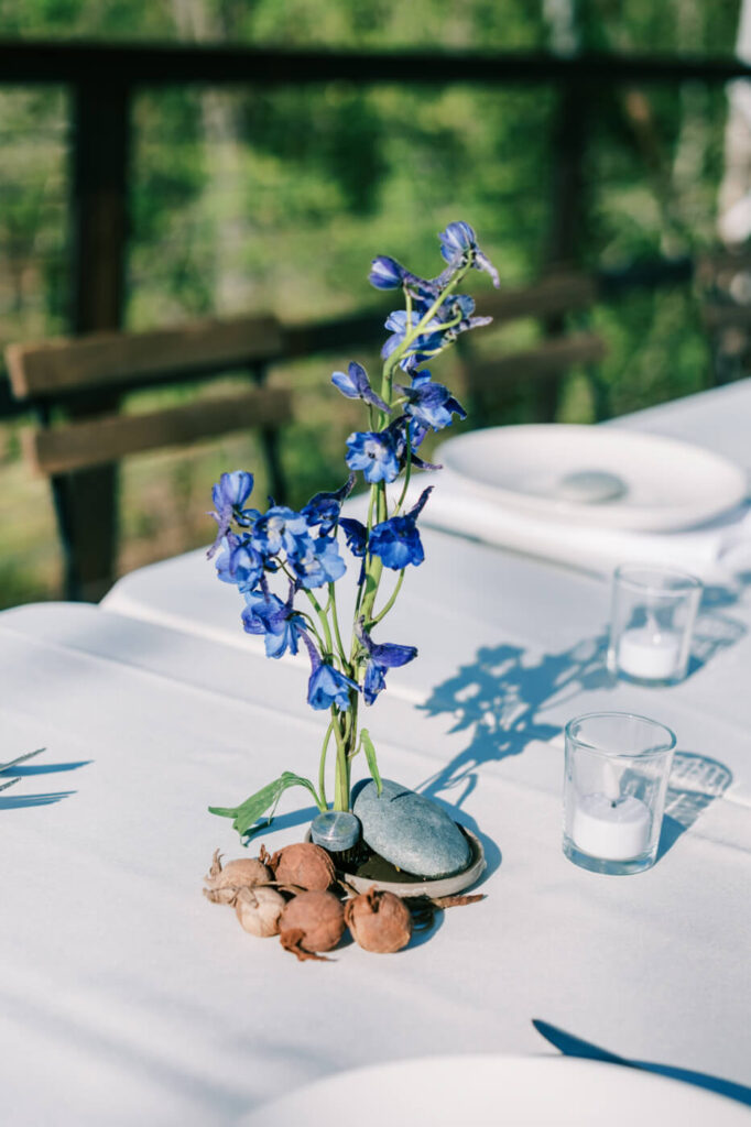 Minimalist floral arrangement at Finley Farms Bridge – A single blue delphinium in a modern rock arrangement, accompanied by votive candles on the rehearsal dinner table.