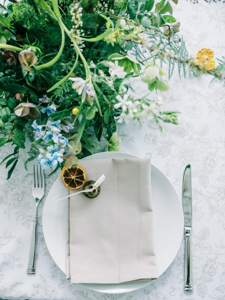 Elegant wedding table setting at Two Rivers Greenhouse – A close-up of a beautifully styled place setting with a beige napkin, dried citrus garnish, and delicate floral accents at a Two Rivers Greenhouse wedding in Missouri.