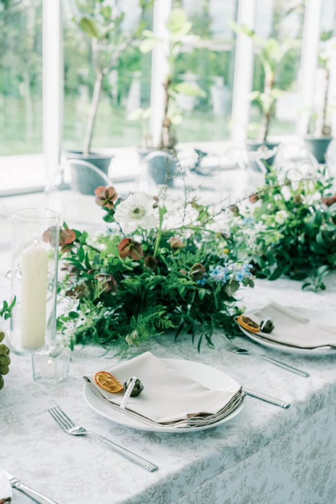 Lush floral tablescape at Two Rivers Greenhouse wedding – A stunning tablescape adorned with fresh greenery, blue and white blooms, and candlelit accents inside the sunlit glass venue of Two Rivers Greenhouse.