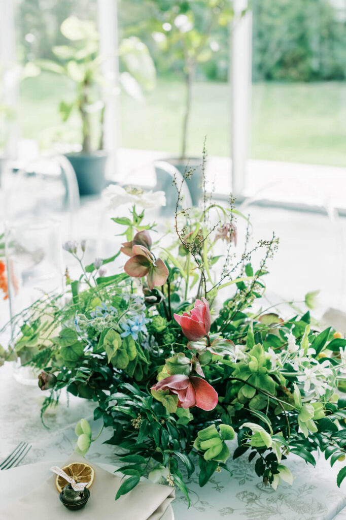 Romantic wedding centerpiece at Two Rivers Greenhouse – A lush floral arrangement with deep red and green foliage, white anemones, and delicate blue flowers, creating an organic and romantic aesthetic at a Two Rivers Greenhouse wedding.