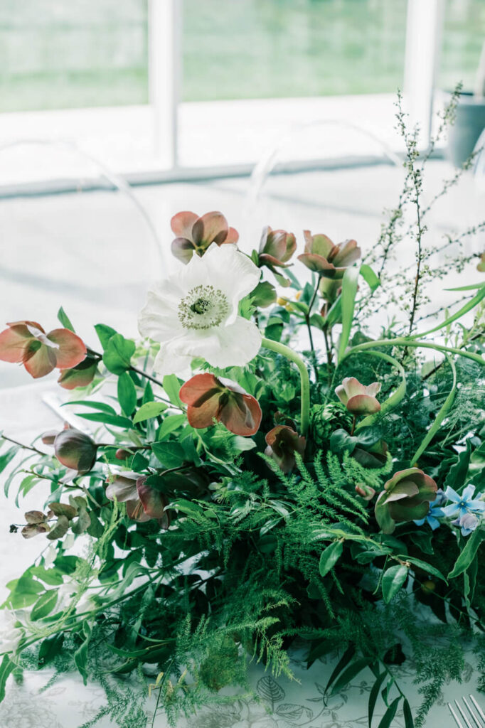 Fine art floral design for a Two Rivers Greenhouse wedding – A close-up of an intricate wedding floral arrangement with fresh greenery, blue flowers, and burgundy accents, capturing the botanical beauty of Two Rivers Greenhouse.