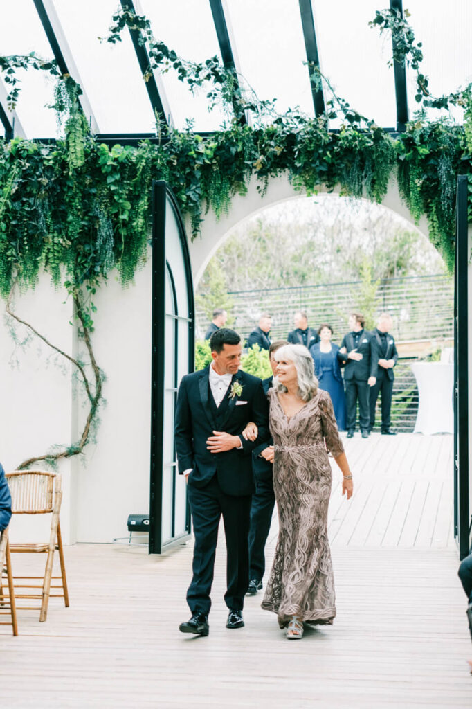 Groom walks down the aisle at Greenhouse Two Rivers wedding – image of the groom and his mother walking down the aisle at Greenhouse Two Rivers.