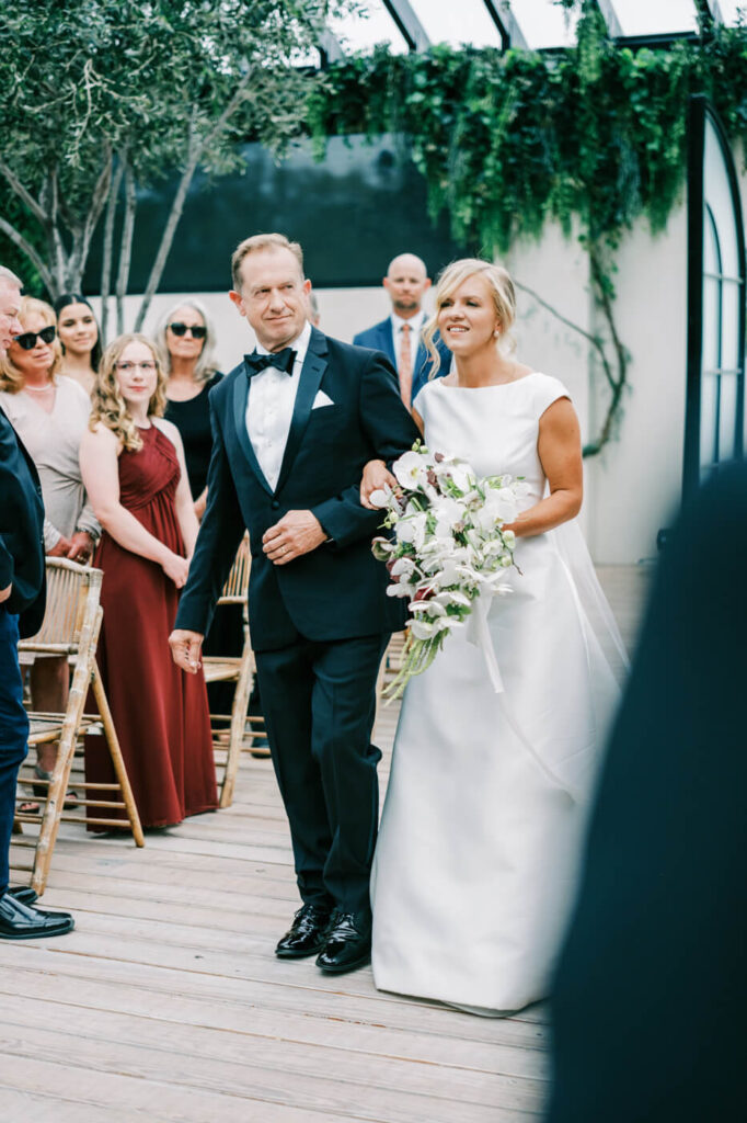 Father walking bride down the aisle at Greenhouse Two Rivers wedding – A joyful moment as the father of the bride escorts his daughter down the aisle, surrounded by guests at Greenhouse Two Rivers.