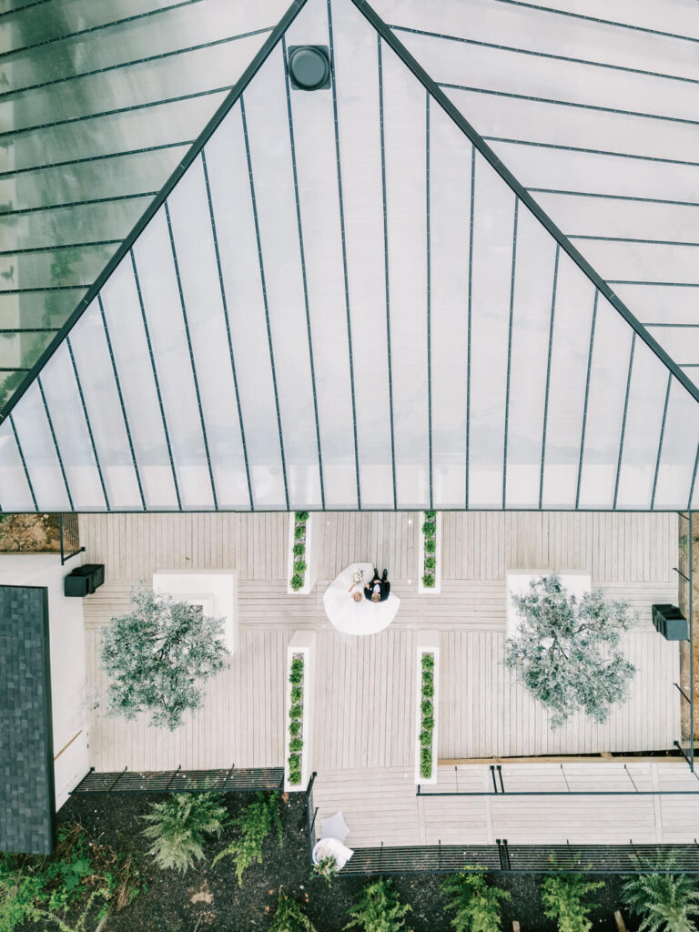 Bride and father entering the ceremony at Greenhouse Two Rivers – A romantic aerial view of the bride and father standing in the courtyard of Greenhouse Two Rivers