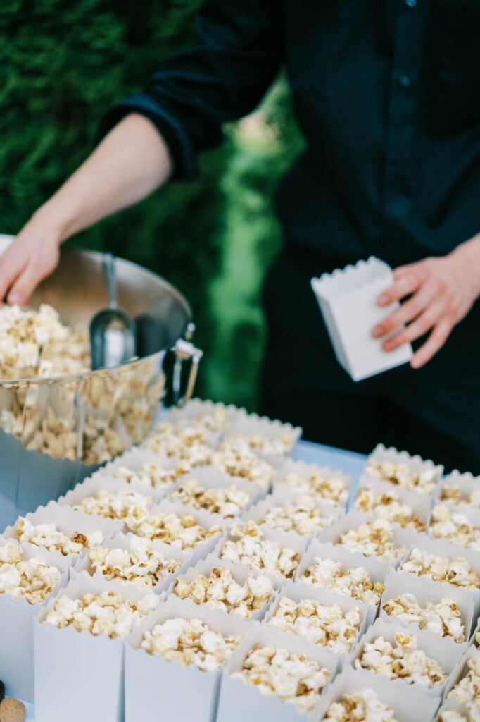 Wedding guest in black uniform scooping caramel popcorn into individual white paper bags for guests.