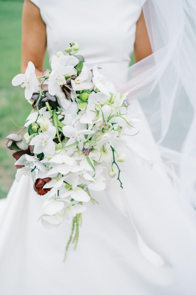 Close-up of bride’s bouquet featuring cascading white orchids, deep burgundy flowers, and trailing greenery.