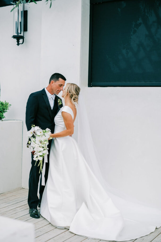 Elegant Bride and Groom Portrait at Greenhouse Two Rivers – The couple shares an intimate moment in front of the modern white architecture of Greenhouse Two Rivers, with the bride's flowing veil and groom’s black tux adding timeless elegance.