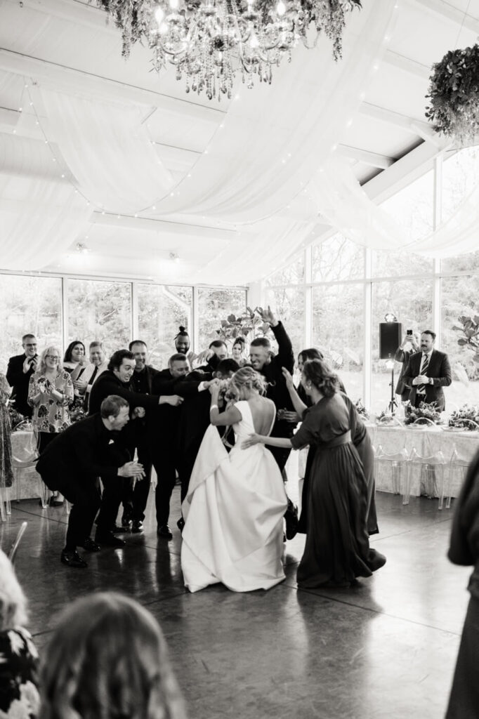 Lively Reception Celebration at Greenhouse Two Rivers – A black-and-white image captures the wedding party and guests surrounding the couple in a joyful, energetic dance inside the elegant Greenhouse Two Rivers venue.