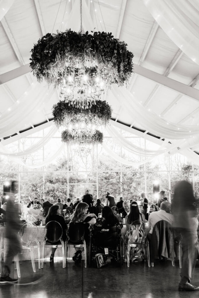 Grand Reception Ambiance at Greenhouse Two Rivers – A dreamy black-and-white image of the wedding reception, featuring cascading greenery chandeliers and twinkling lights in the glass greenhouse at Greenhouse Two Rivers.