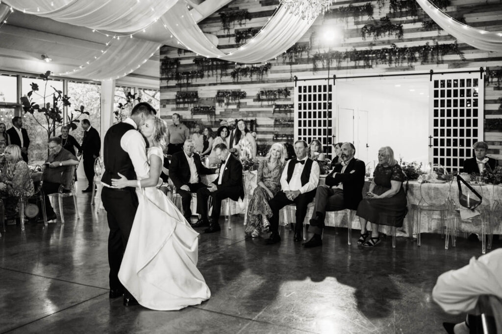 Romantic First Dance Scene - The bride and groom share an intimate first dance as wedding guests watch, with draped fabric and fairy lights creating a dreamy ambiance.