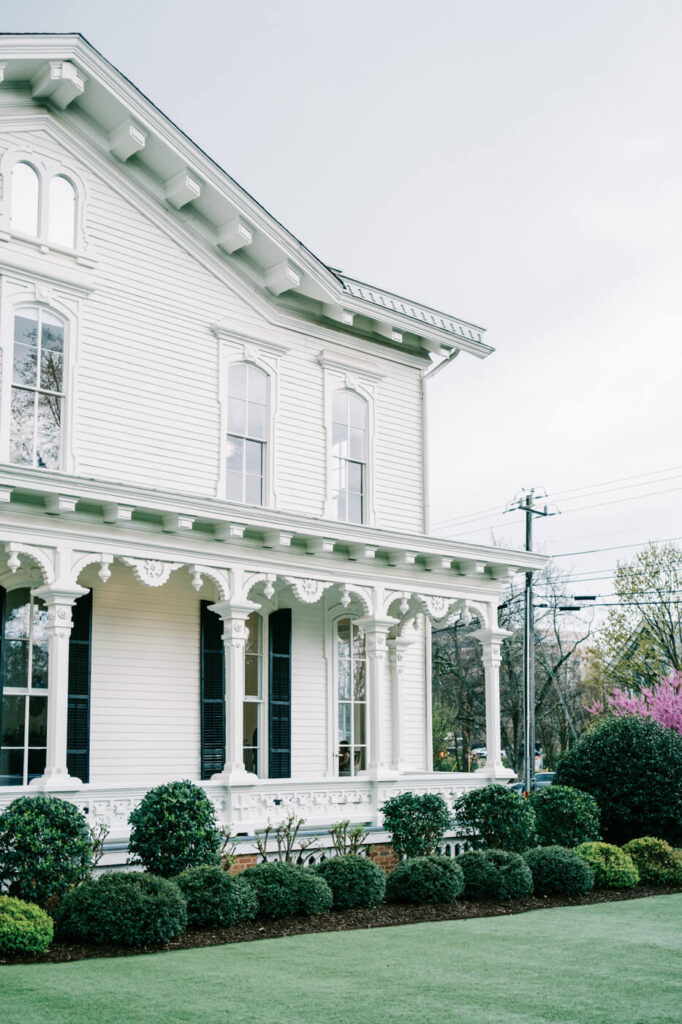 Side view of the historic Merrimon-Wynne House in Raleigh, featuring white columns and a wraparound porch on a rainy spring day.