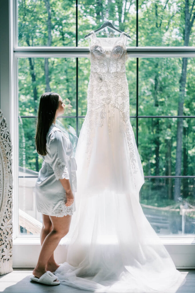 Bride Bonnie admiring her wedding dress in front of the grand window at Carolina Grove, bathed in natural light.