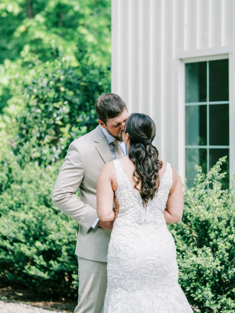 Close-up of the bride and groom’s first kiss outside Carolina Grove, surrounded by greenery and elegant wedding details.