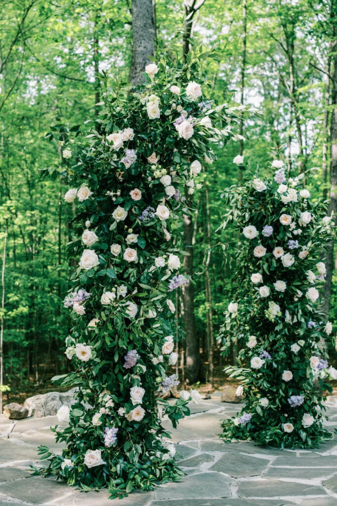 Elegant floral arch of white and blush roses with greenery, set in front of the Carolina Grove forest for a romantic ceremony backdrop.