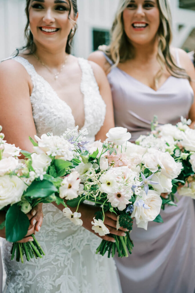 Bride smiling with bridesmaids, holding lush bouquets of white, blush, and lavender flowers at Carolina Grove.